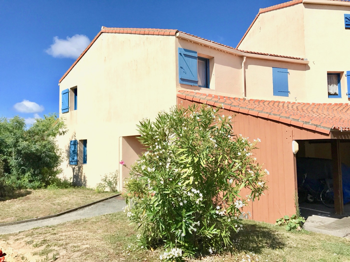 The exterior of B26, a sandy-coloured duplex with blue shutters and an oleander in the garden
